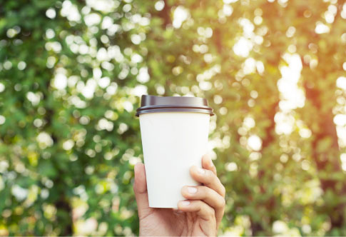 An image of an aqueous cup placed in front of lush green trees, highlighting its eco-friendly nature. Aqueous cups are a sustainable alternative to traditional cups, featuring a water-based coating instead of plastic, making them fully recyclable and biodegradable. Perfect for businesses looking to reduce their environmental impact while still enjoying high-quality, durable packaging.